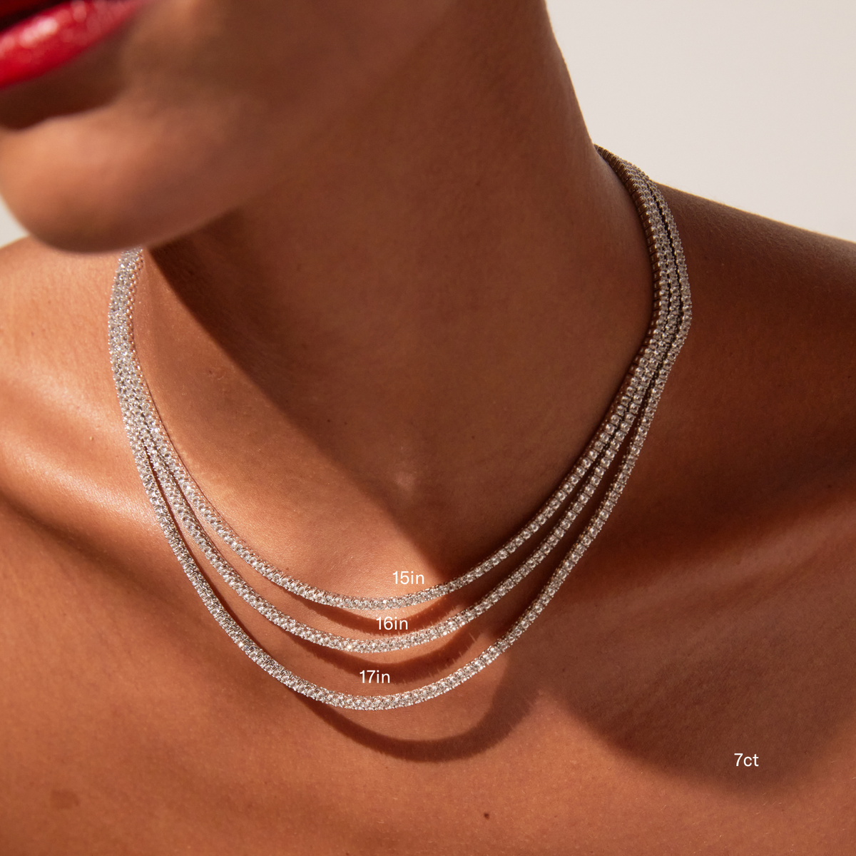 Model. Close-up of a woman's neck and lower face featuring bright red lipstick, wearing three layered white sapphire tennis necklaces. The image includes text overlays labeling the necklace lengths as 15in, 16in, and 17in, and indicates a 7ct weight in the bottom corner.