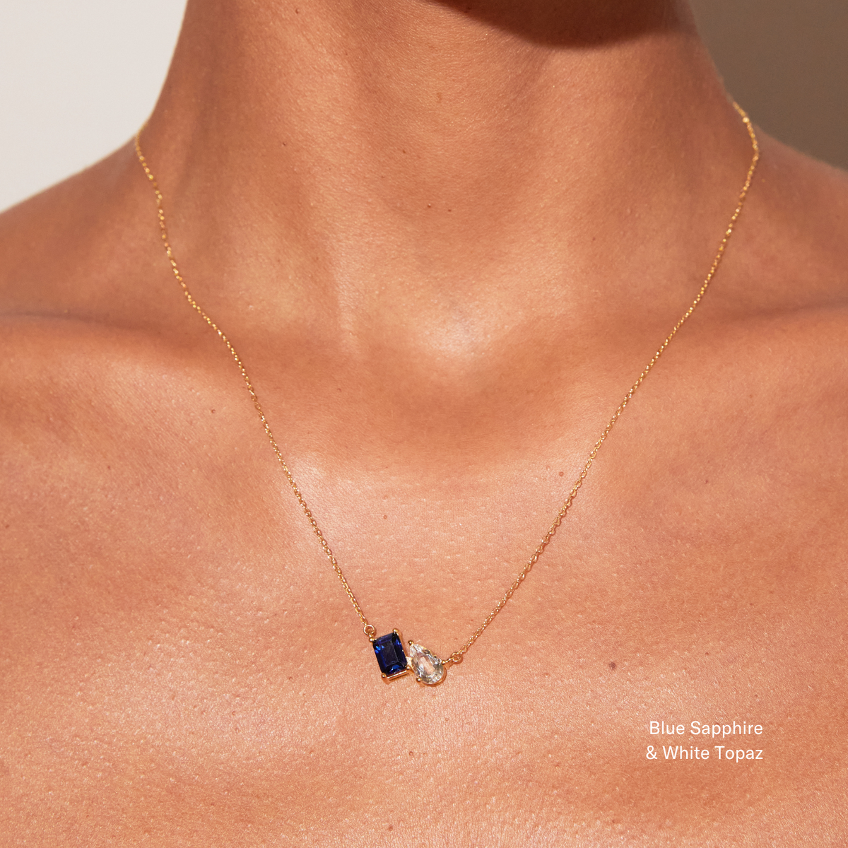 Model Woman wearing a gold necklace with a blue sapphire and white topaz pendant