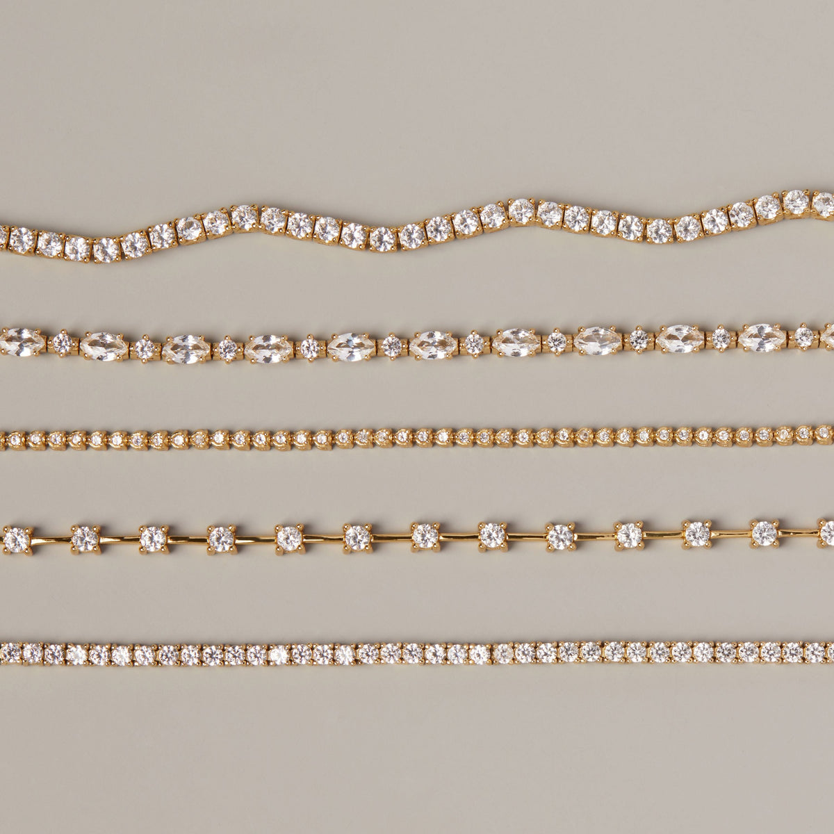 Model. Five different styles of gold diamond tennis necklaces arranged horizontally on a neutral beige background.