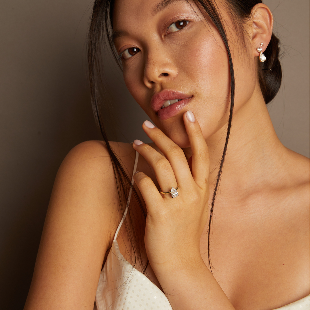 Model. Woman wearing a ring and pearl earrings against a neutral background