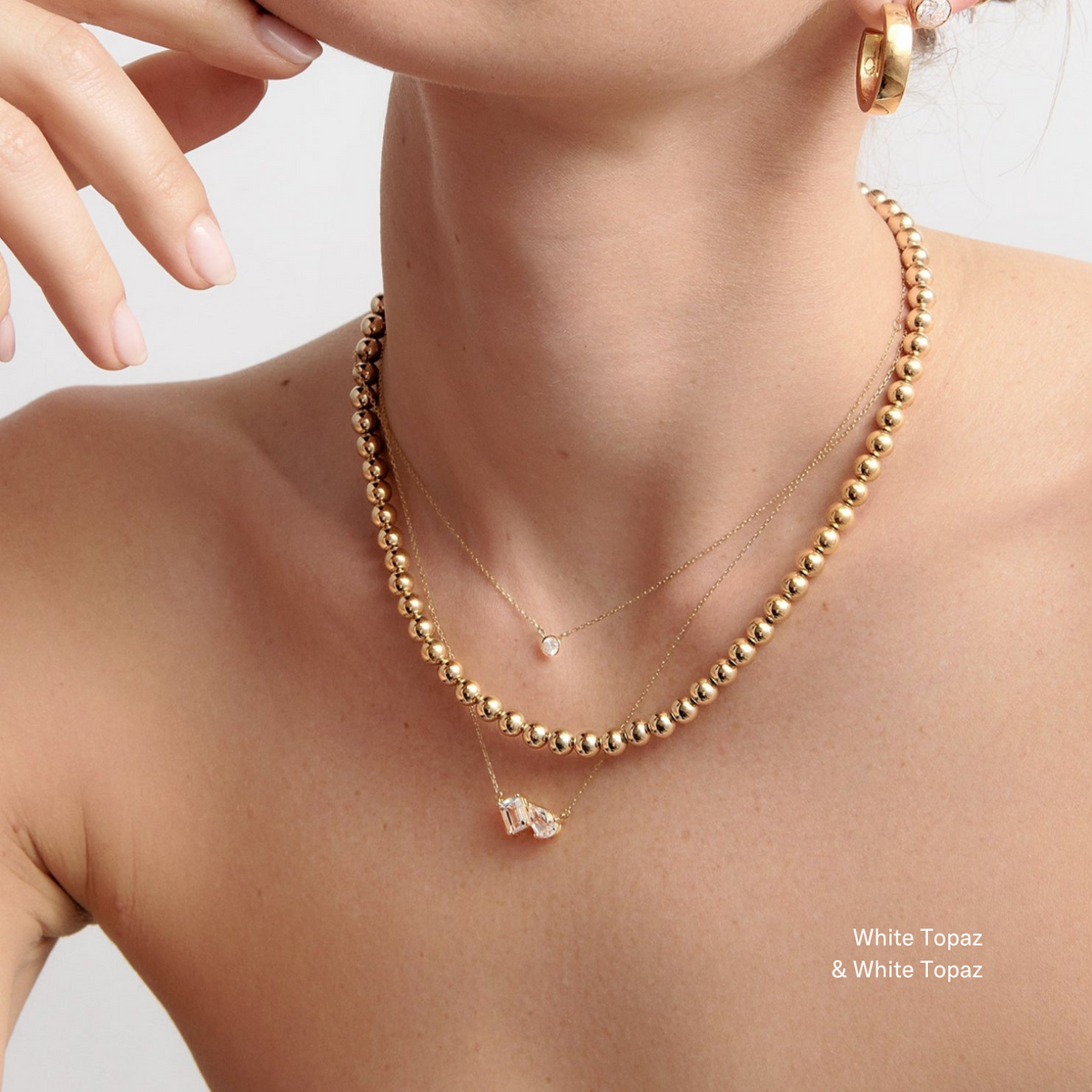 Model Woman wearing layered gold necklaces, including a double white topaz pendant
