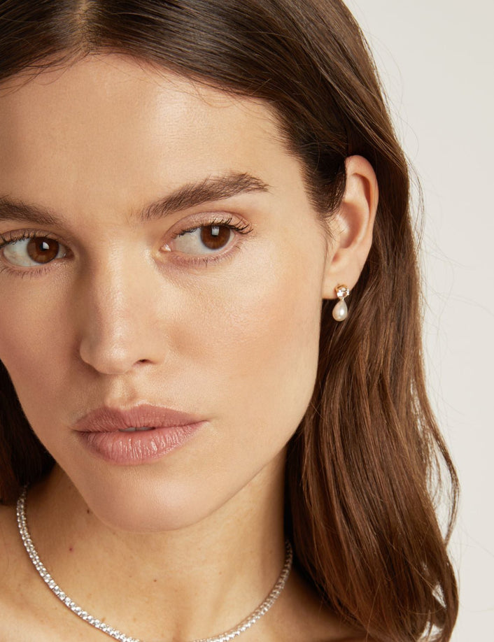Model. Close-up of a woman wearing a pearl earring and silver necklace on a neutral background