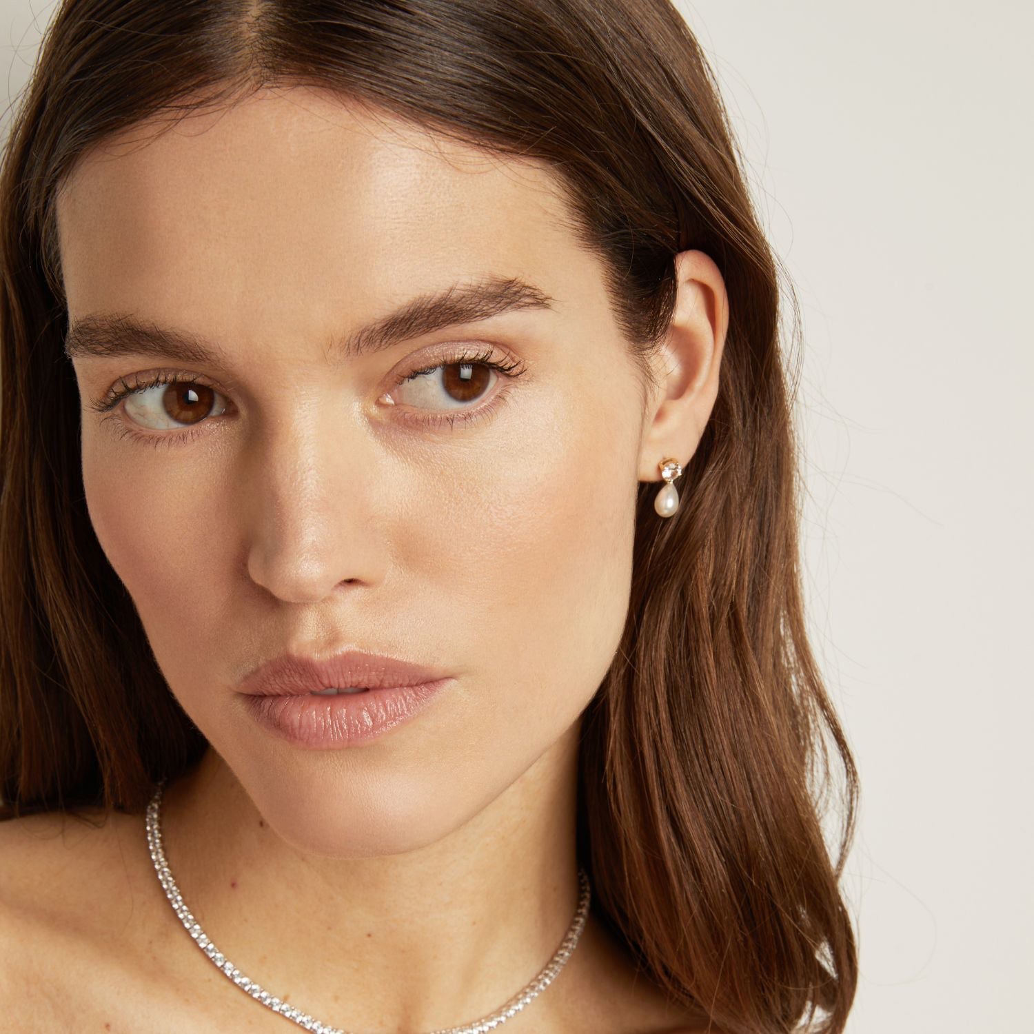 Model. Close-up of a woman wearing a pearl earring and silver necklace on a neutral background