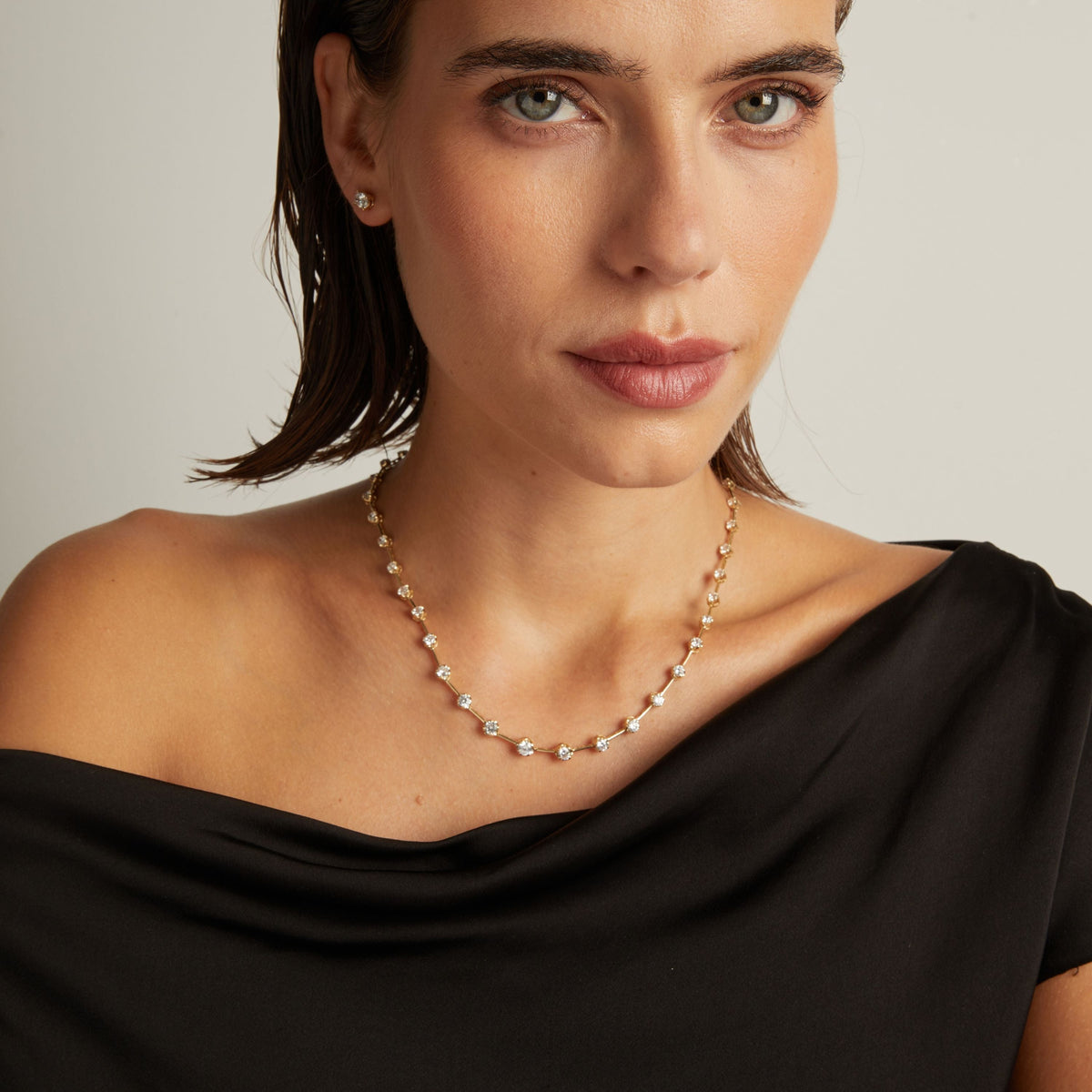 Model. Close up of a woman in a black top wearing a diamond bar necklace on beige background.