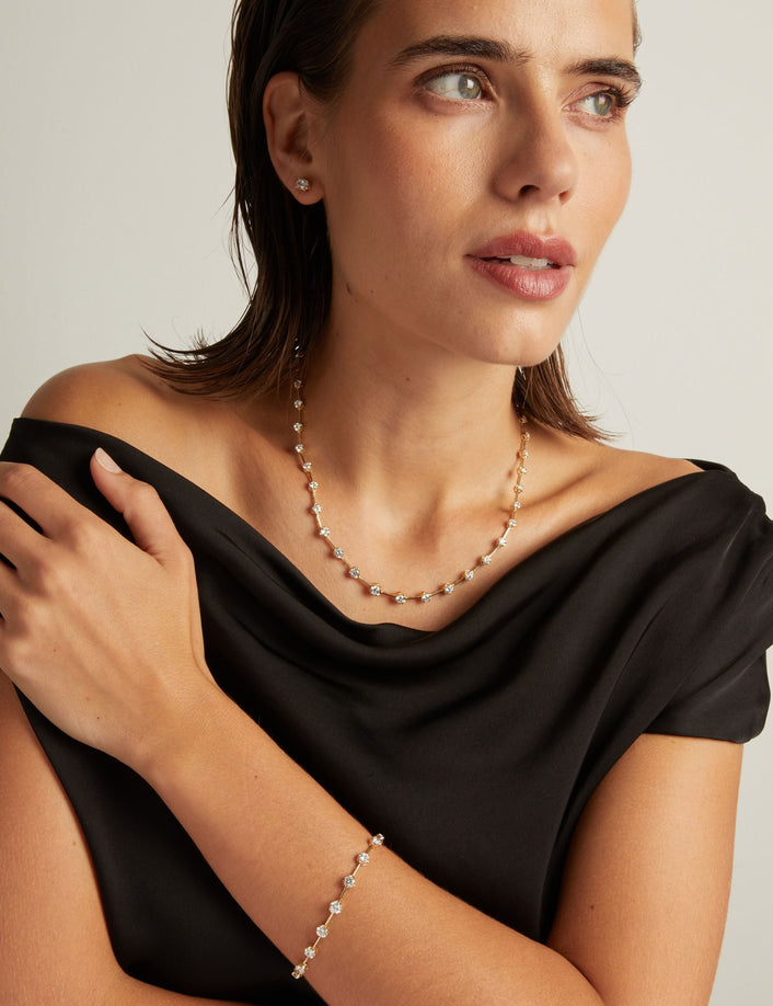 Model. Close up of a woman in a black top wearing a diamond bar necklace and matching bracelet on beige background.