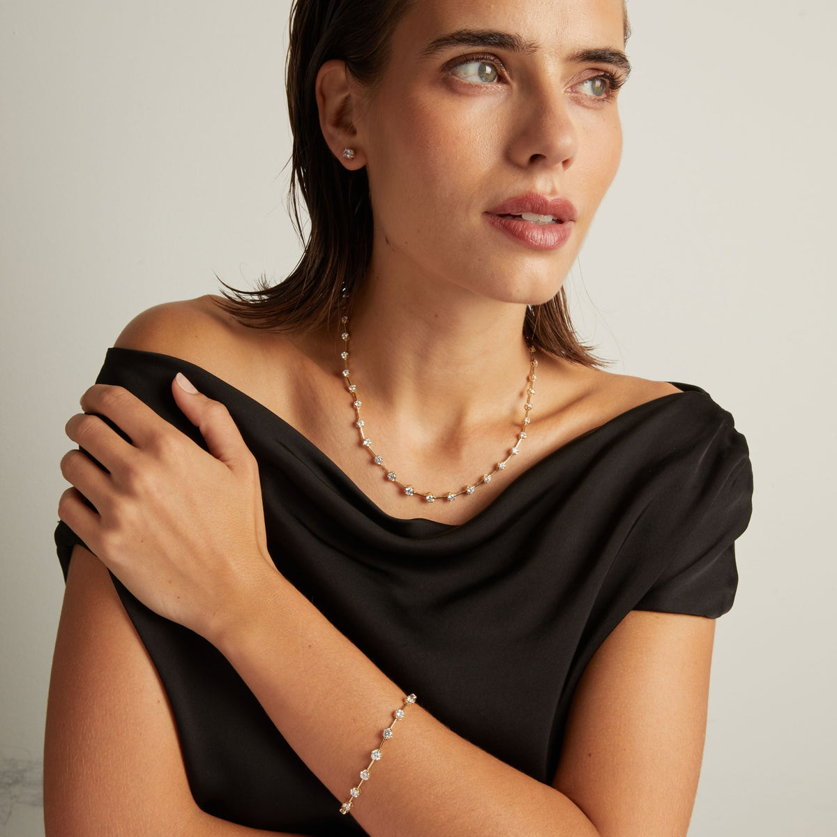 Model. Close up of a woman in a black top wearing a diamond bar necklace and matching bracelet on beige background.