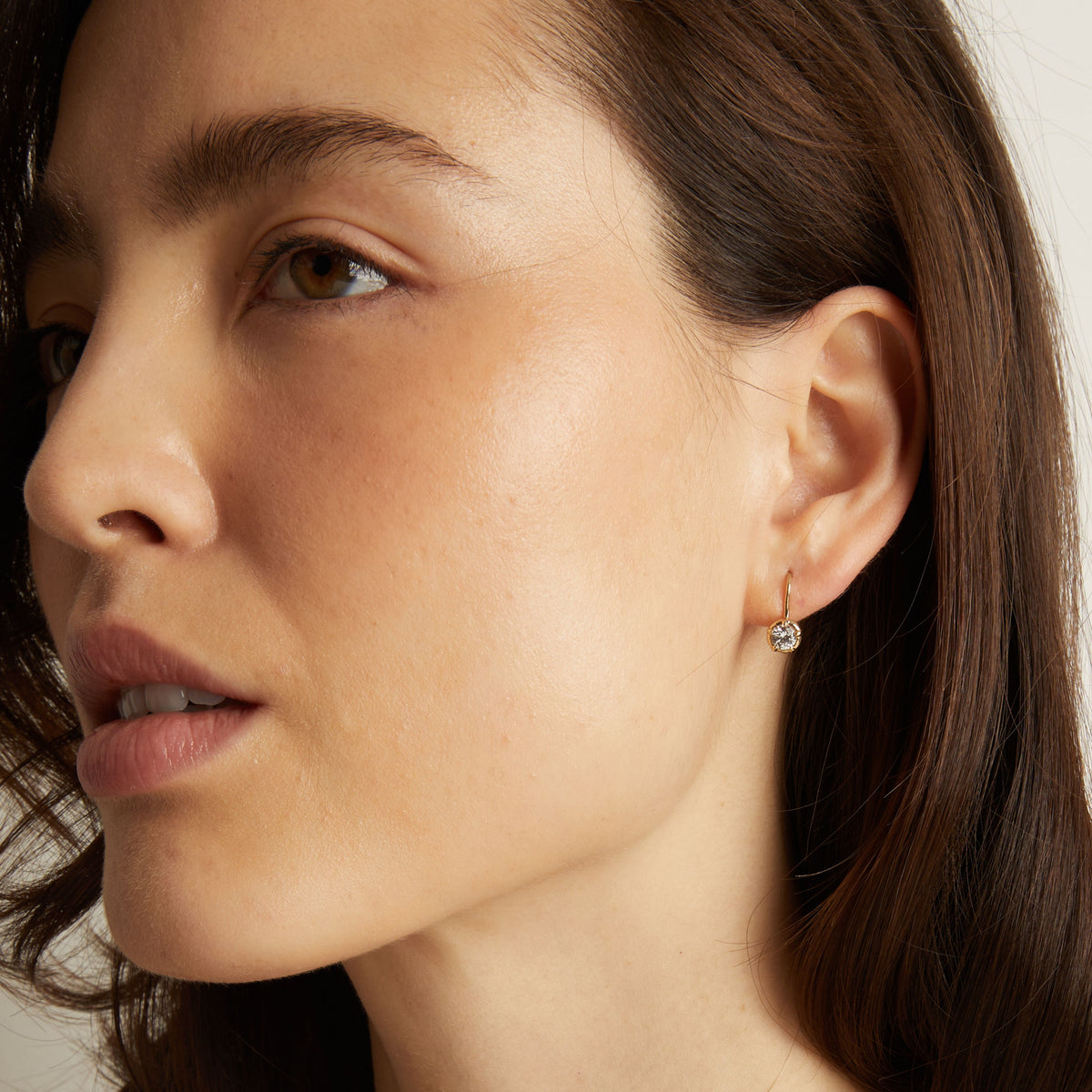 Model. Close-up of a woman wearing a diamond earring with a neutral background