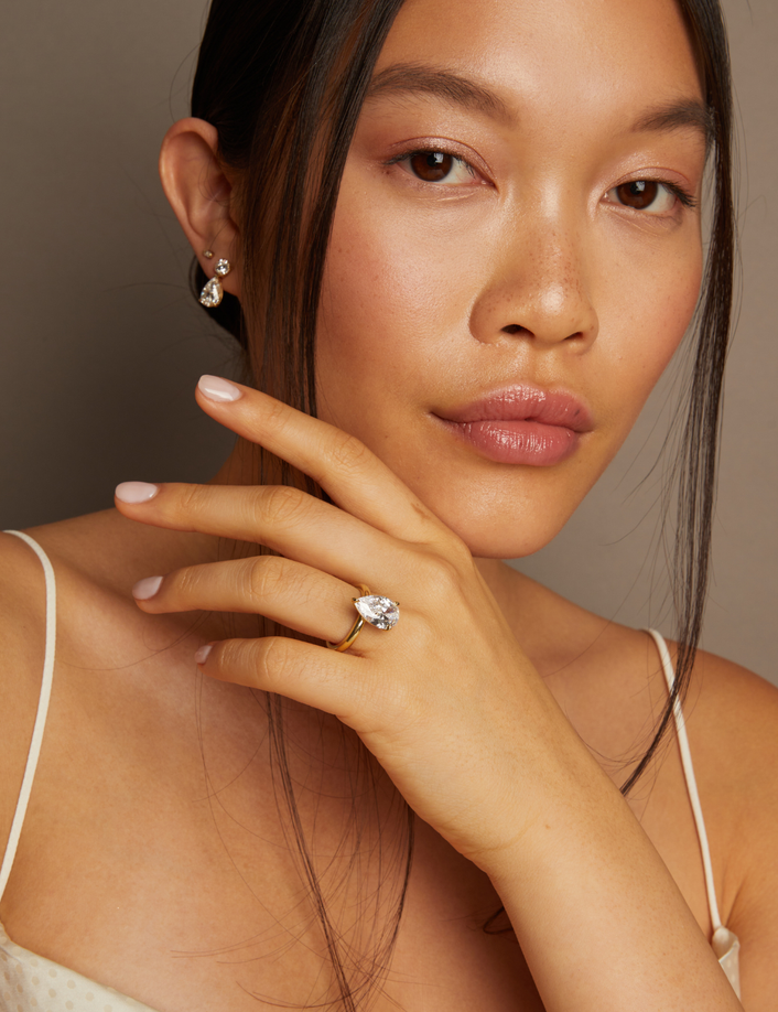 Model. Woman wearing a diamond ring and earrings against a neutral background