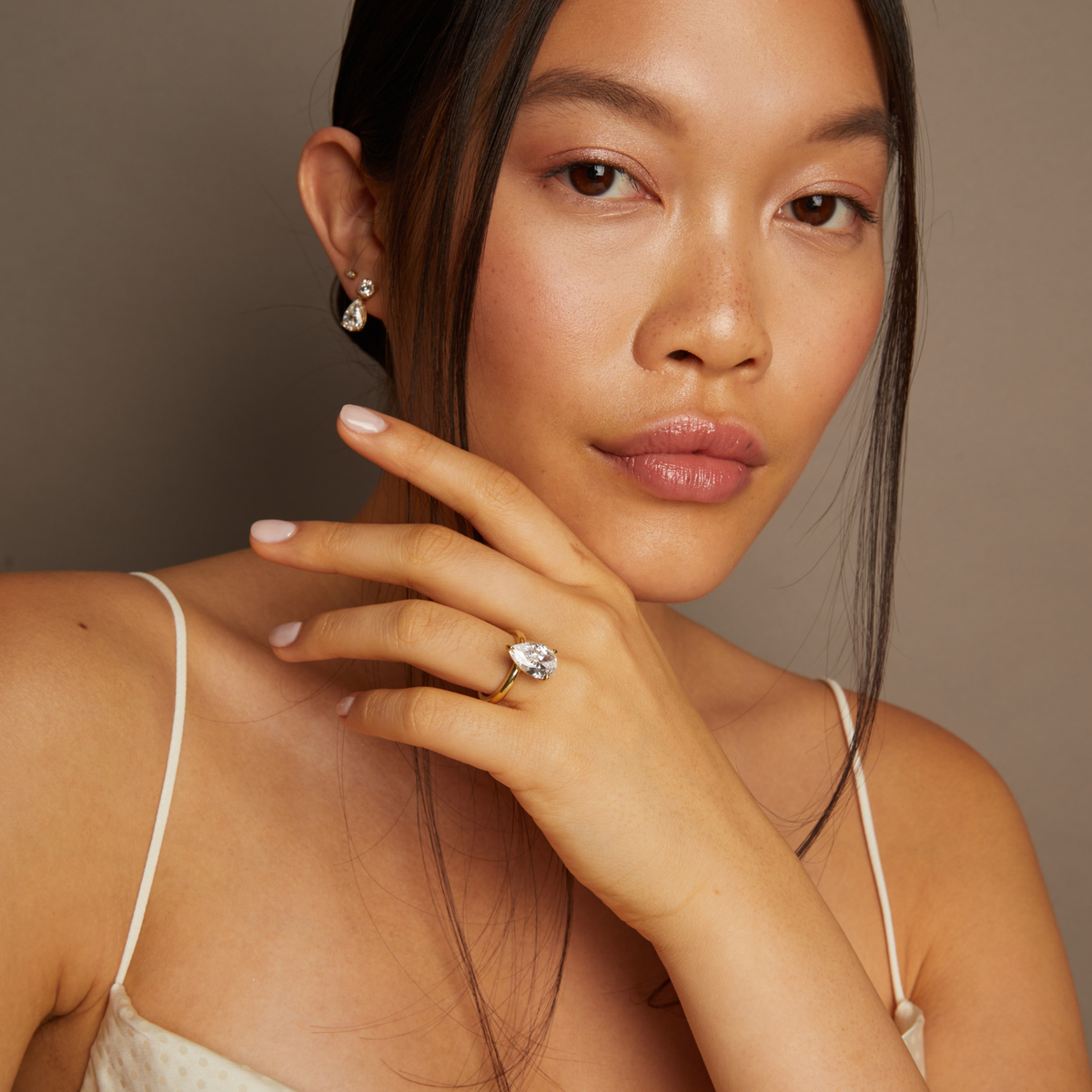 Model. Woman wearing a diamond ring and earrings against a neutral background