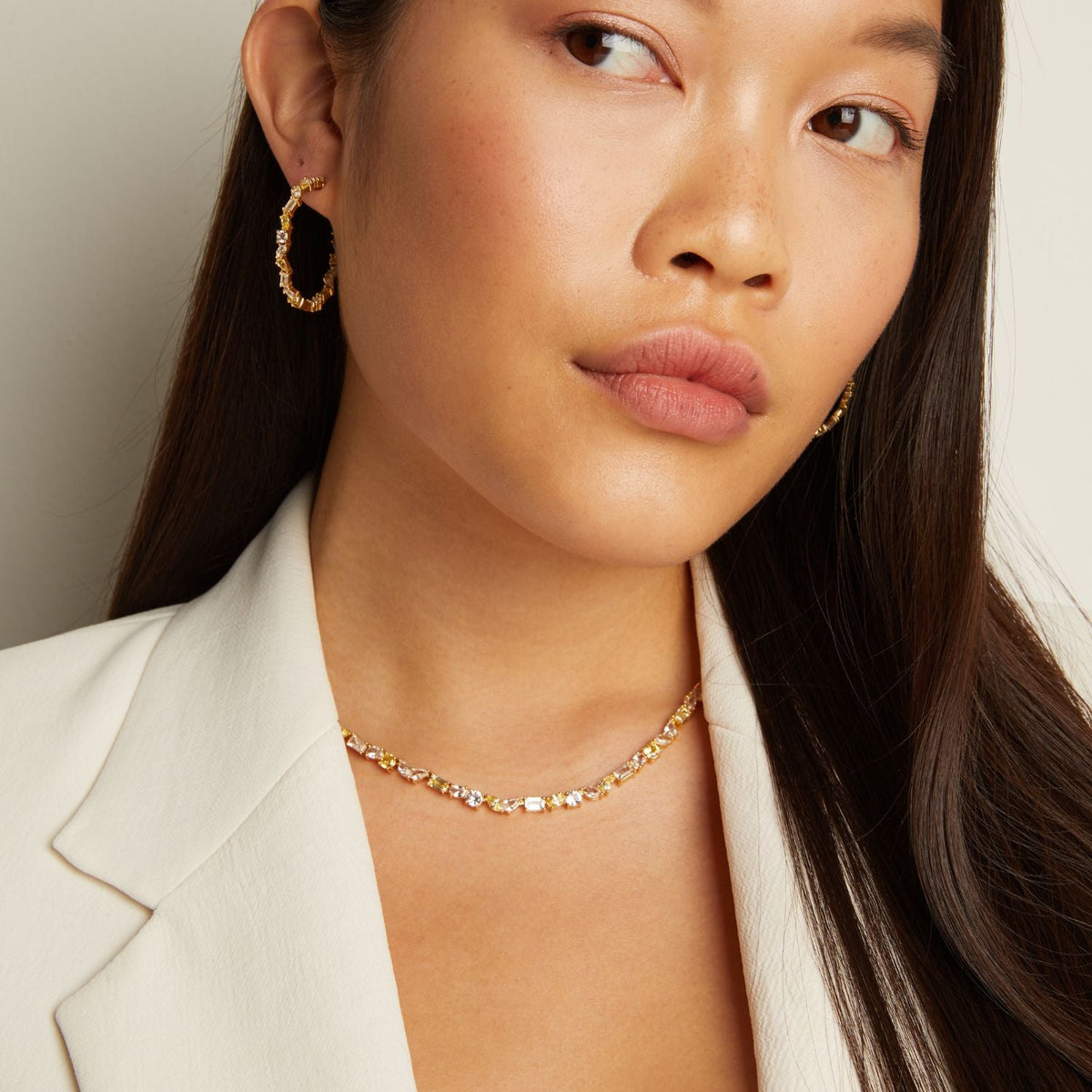 Model. Woman wearing a gold necklace and hoop earrings against a neutral background