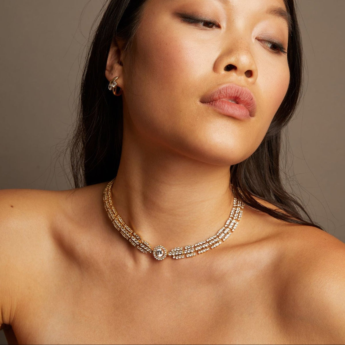 Model. Woman wearing a gold necklace against a neutral background