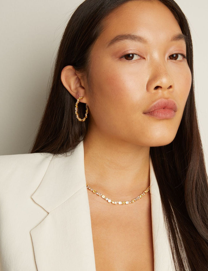 Model. Woman wearing gold earrings and necklace against a neutral background