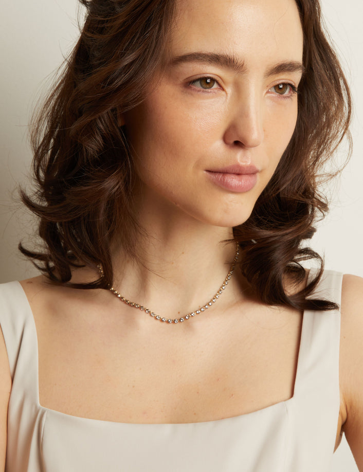 Model. Woman wearing a light-colored top and necklace against a neutral background