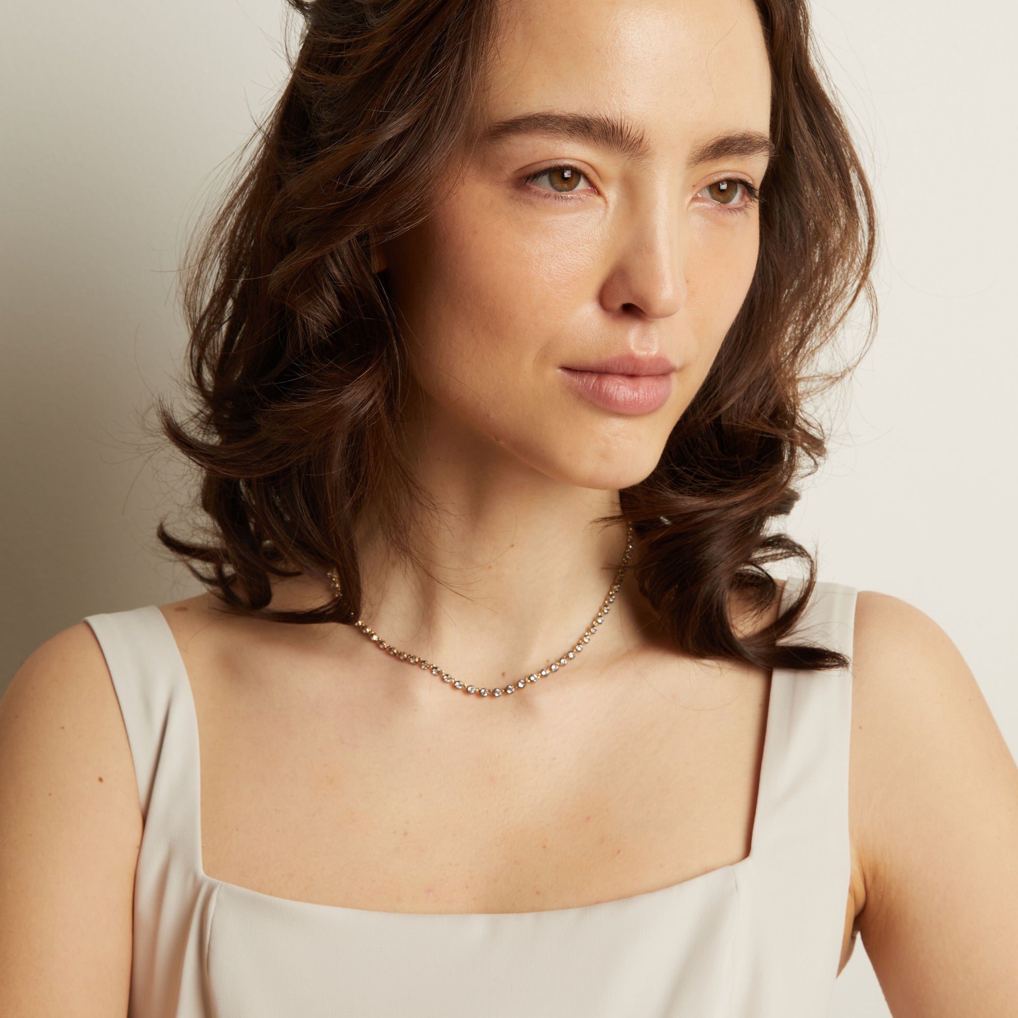 Model. Woman wearing a light-colored top and necklace against a neutral background