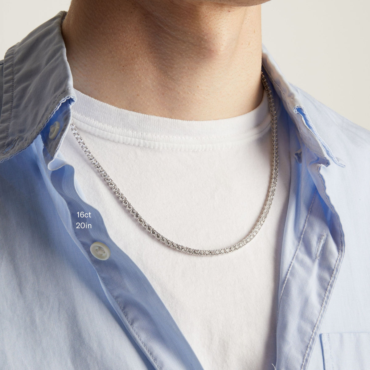 Model. A close-up of a man wearing a tennis necklace over a white t-shirt and a light blue button-down shirt.