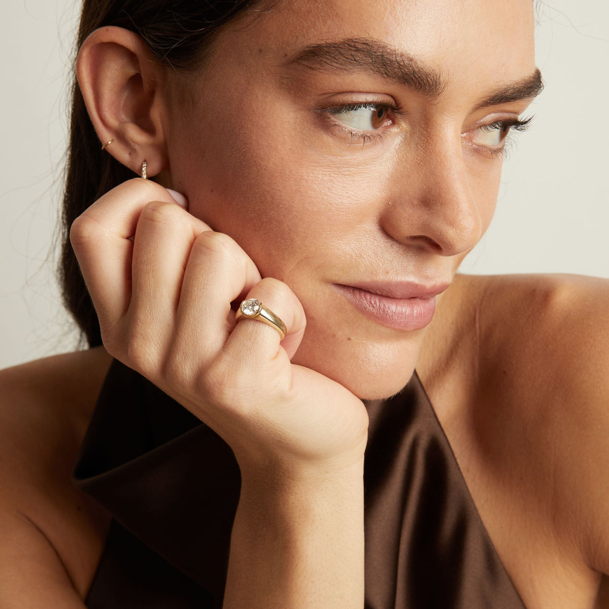 Model. A close-up lifestyle shot of a woman wearing a gold signet ring with a round diamond. 