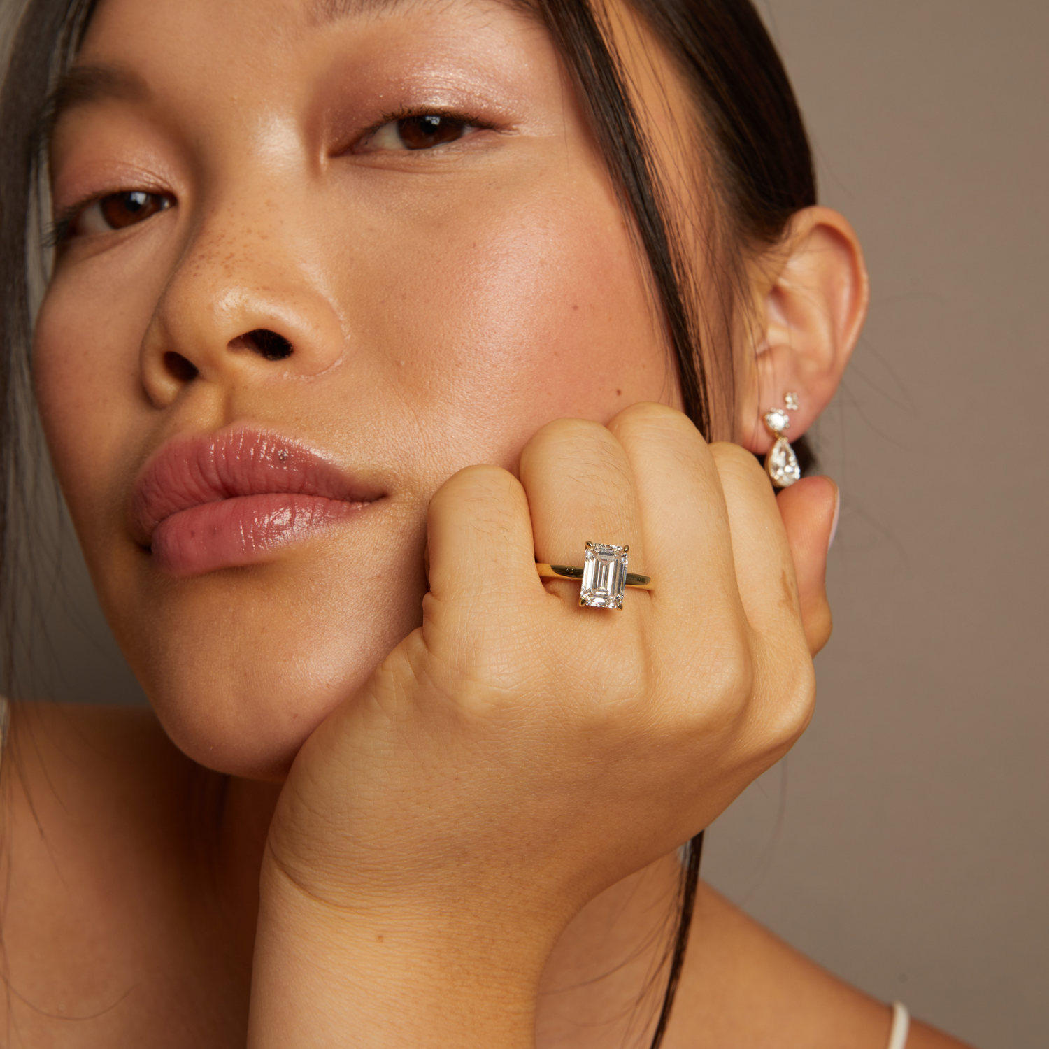 Model. Close-up of a woman wearing a diamond ring and earrings against a neutral background
