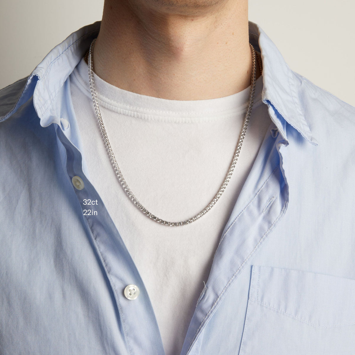 Model. A close-up of a man wearing a tennis necklace over a white t-shirt and a light blue button-down shirt.