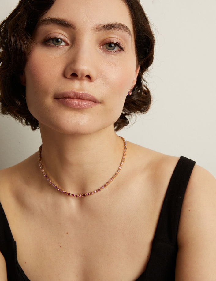 Woman wearing a pink tennis necklace against a neutral background. Model
