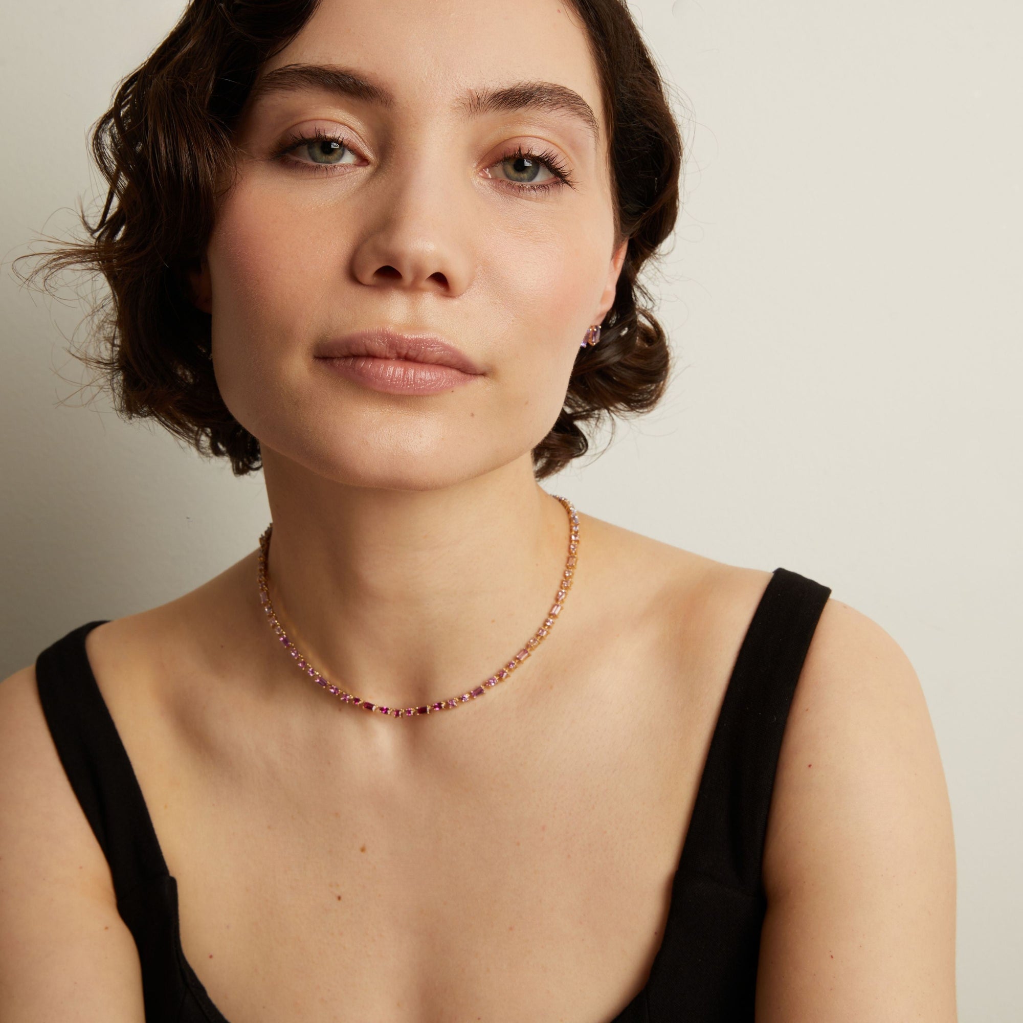 Woman wearing a pink tennis necklace against a neutral background. Model