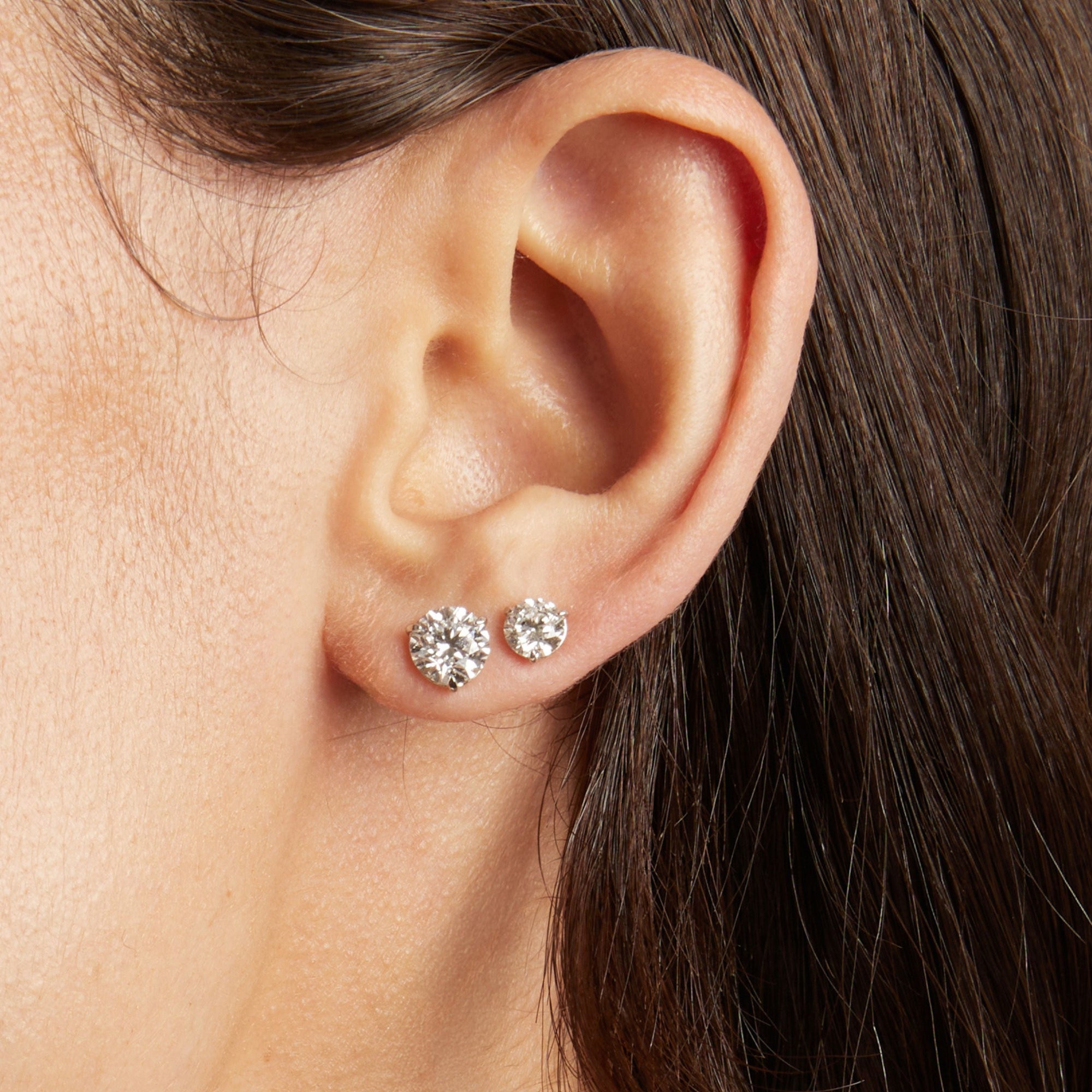 Close up of a woman's ear wearing two diamond stud earrings. 