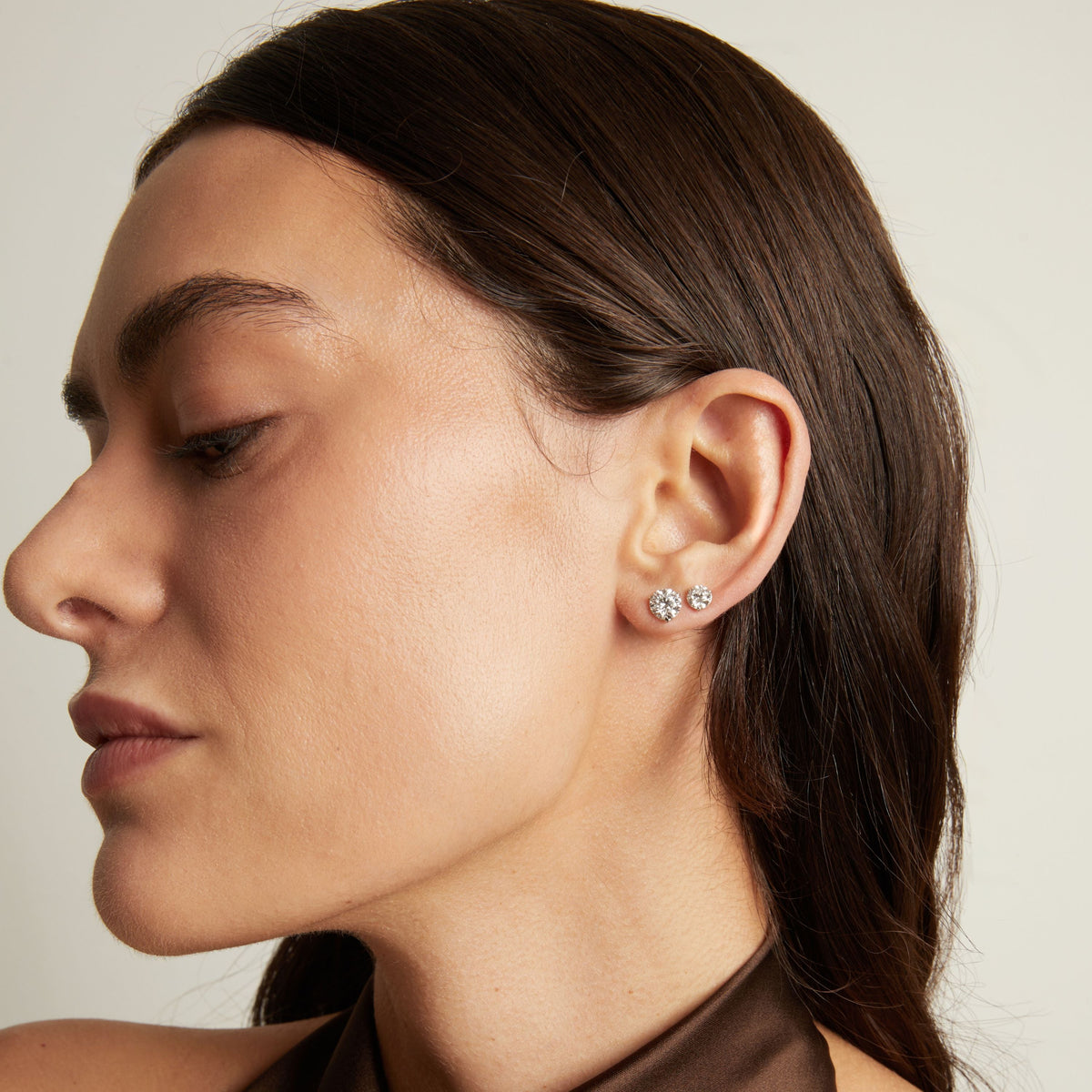 Model. Close up of a woman wearing two diamond stud earrings. 