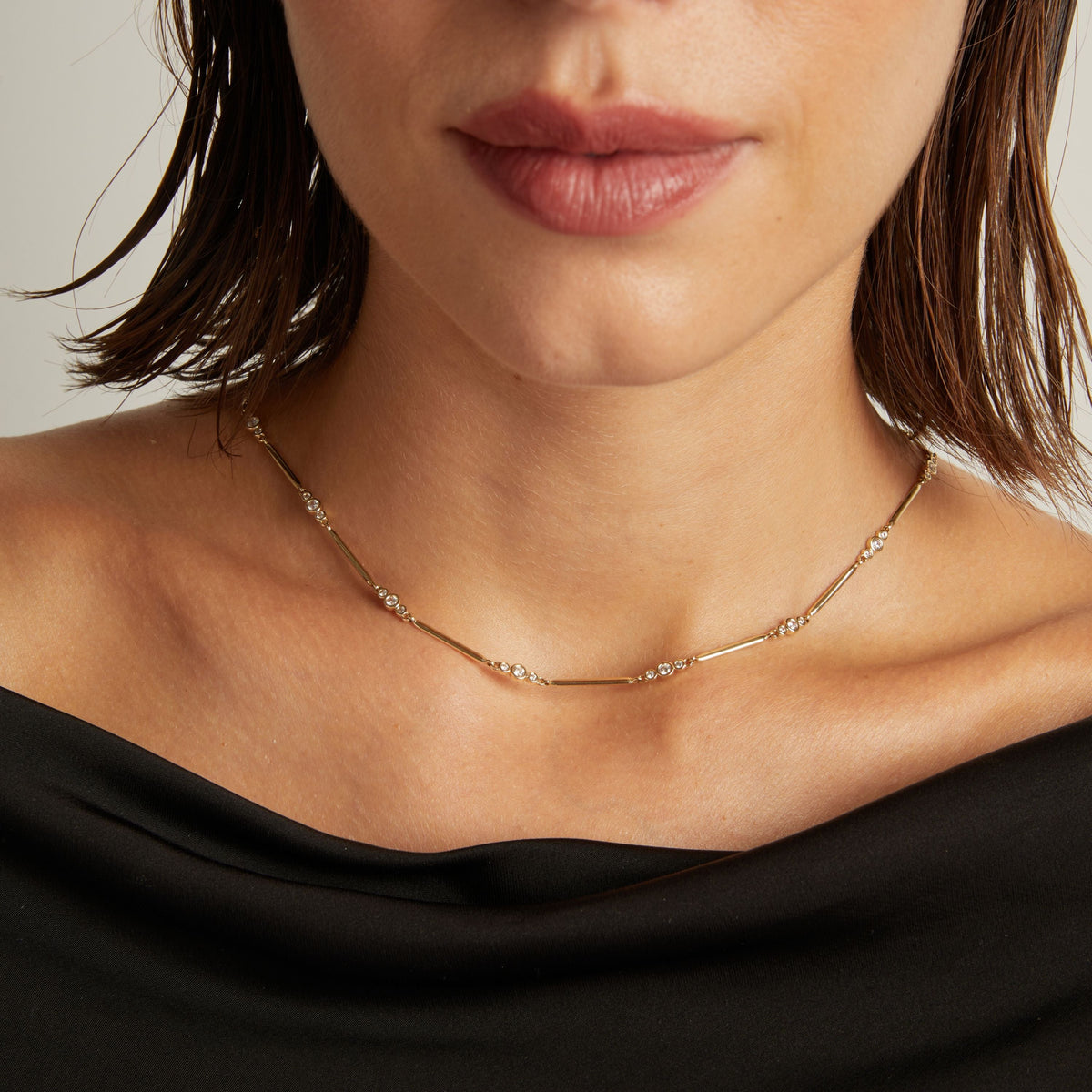 Model. Close up of a woman in a black top wearing a diamond bar necklace on beige background.