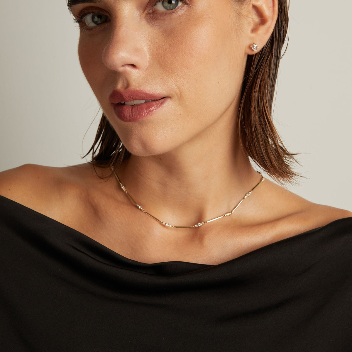 Model. Close up of a woman in a black top wearing a diamond bar necklace on beige background.