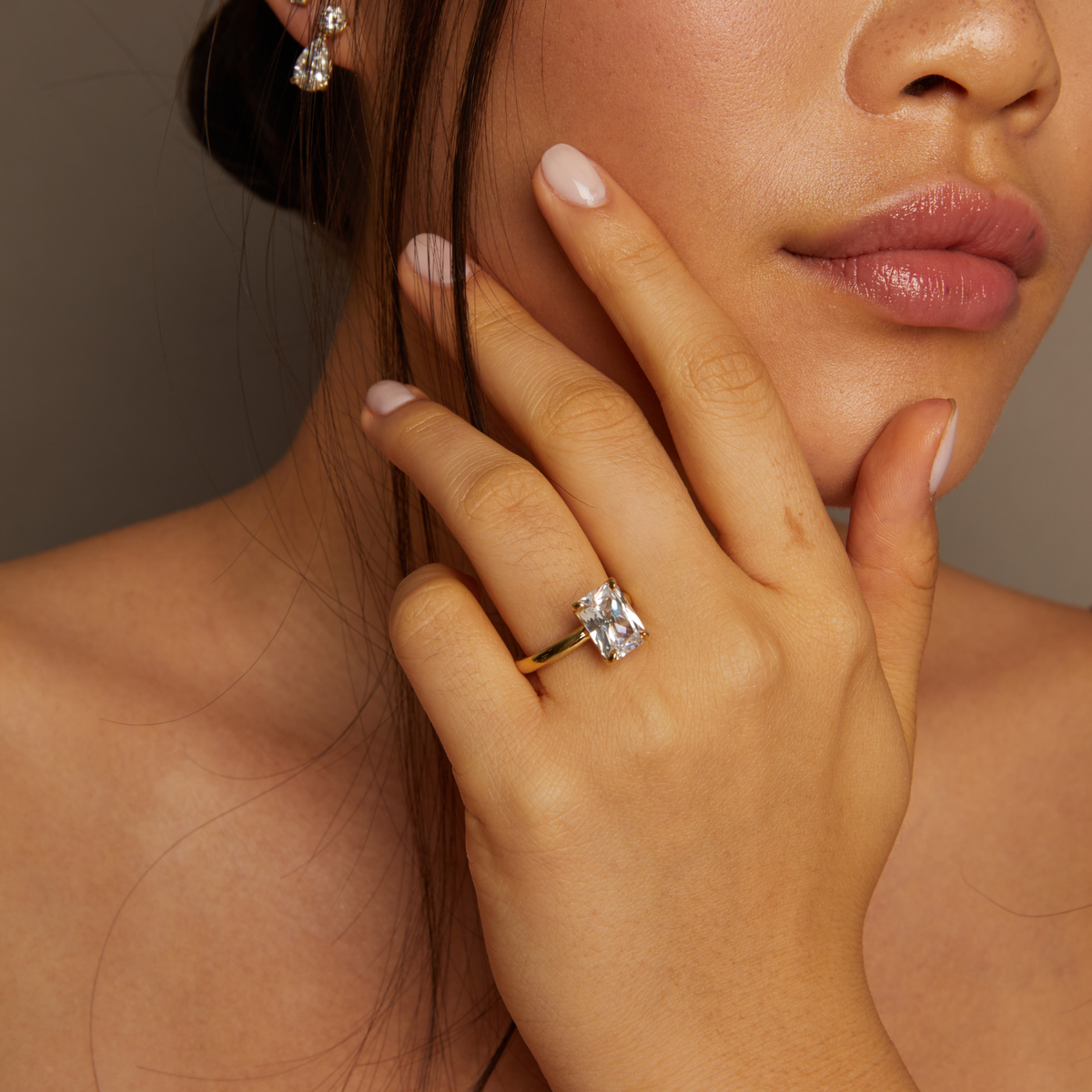 Model. Close-up of a woman's hand wearing a gold ring with a diamond, touching her face.