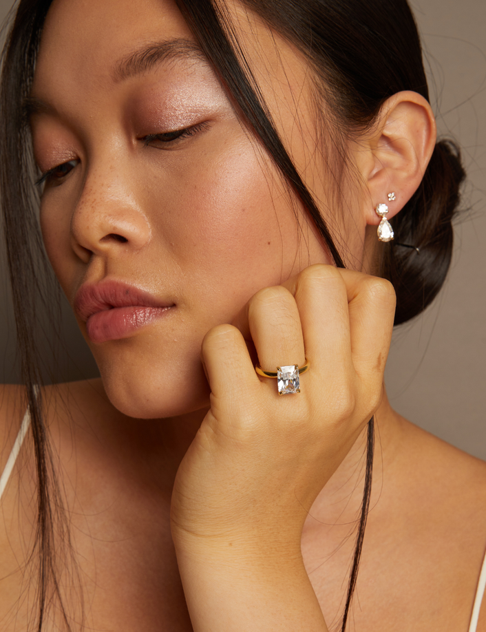 Model. Woman wearing diamond earrings and ring against a neutral background