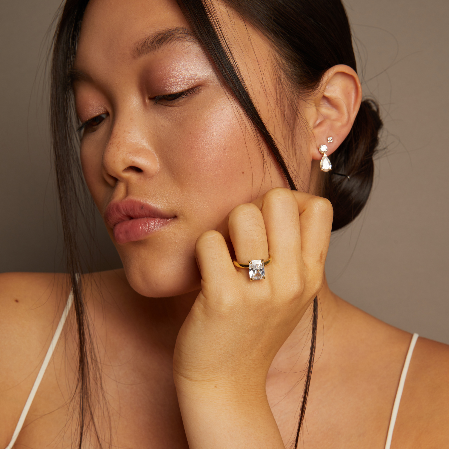 Model. Woman wearing diamond earrings and ring against a neutral background
