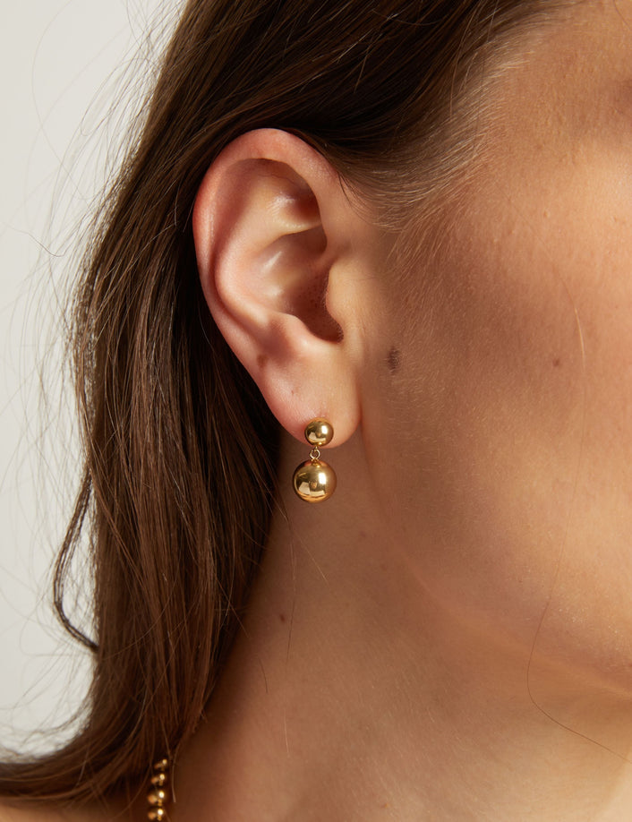 Close up of a person wearing gold earrings with a plain background. 