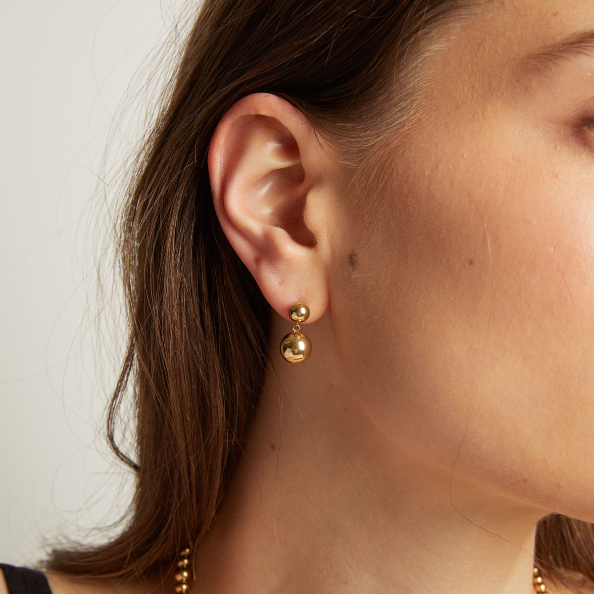 Close up of a person wearing gold earrings with a plain background. 