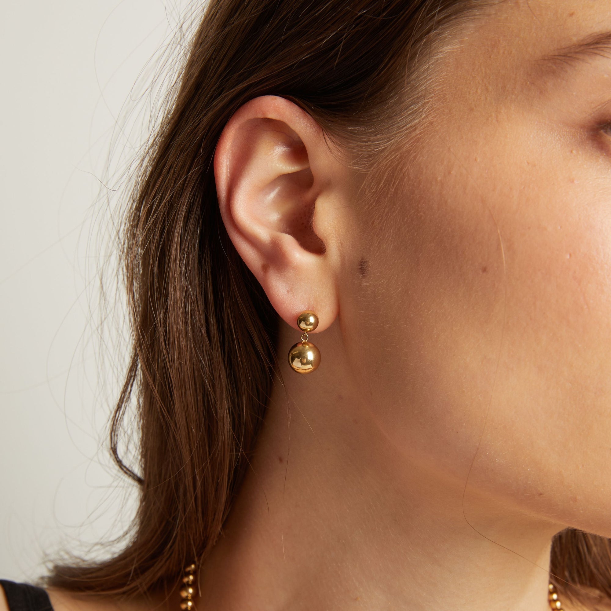 Close up of a person wearing gold earrings with a plain background. 