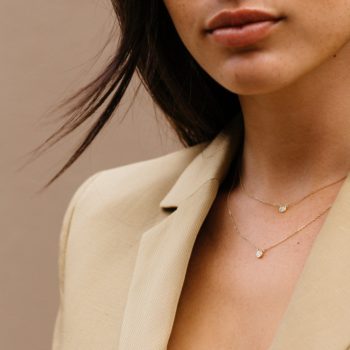 Lifestyle Model. Close up of woman wearing two diamond bezel necklace and beige blazer