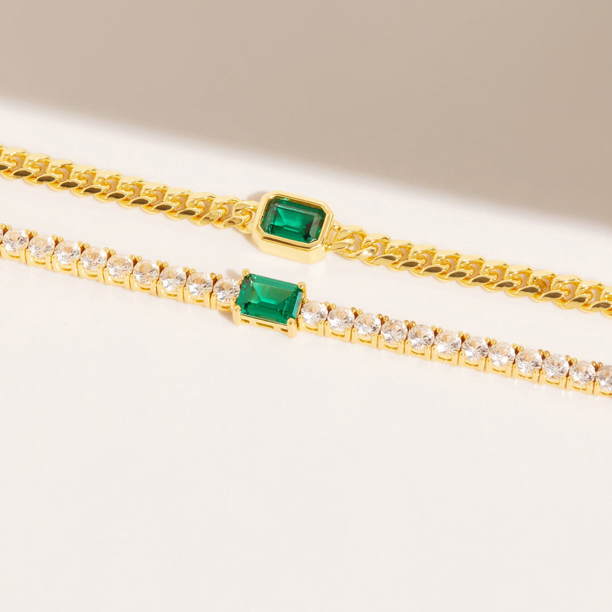 Flatlay Model two diamond chains with an emerald on a white surface 