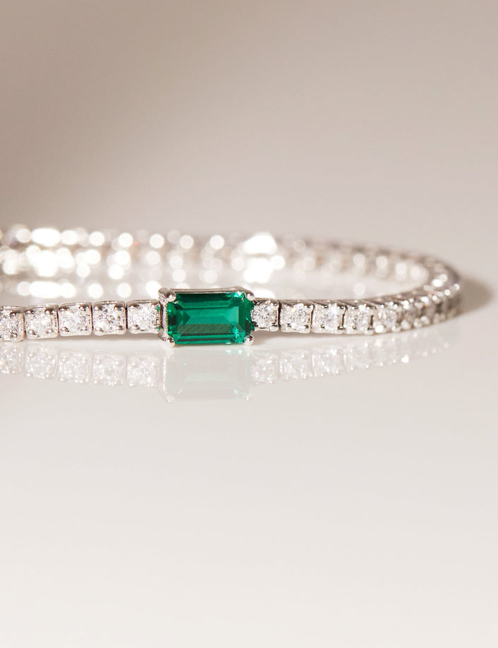 Flatlay Model close up of diamond tennis bracelet with and emerald on a flat surface 