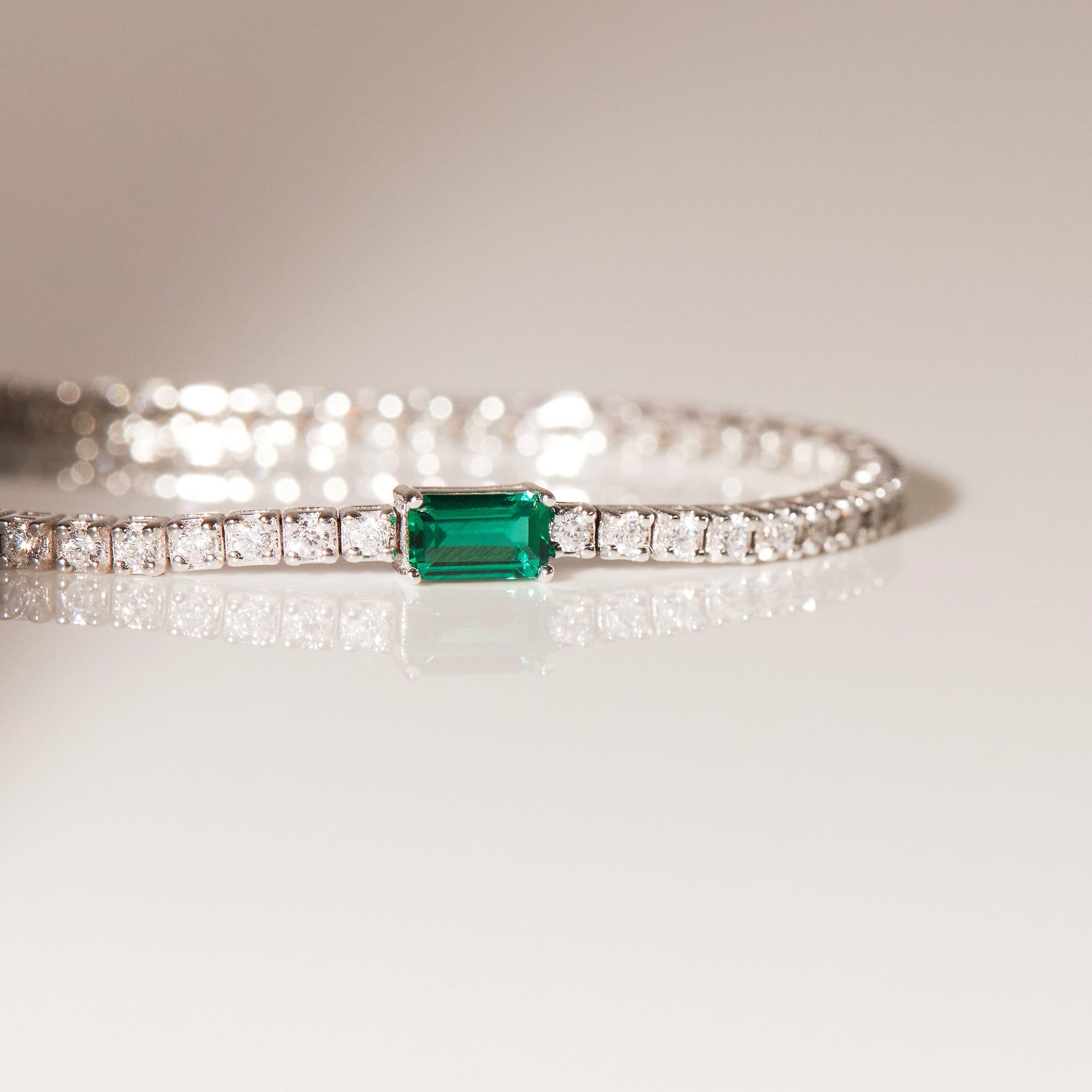 Flatlay Model close up of diamond tennis bracelet with and emerald on a flat surface 