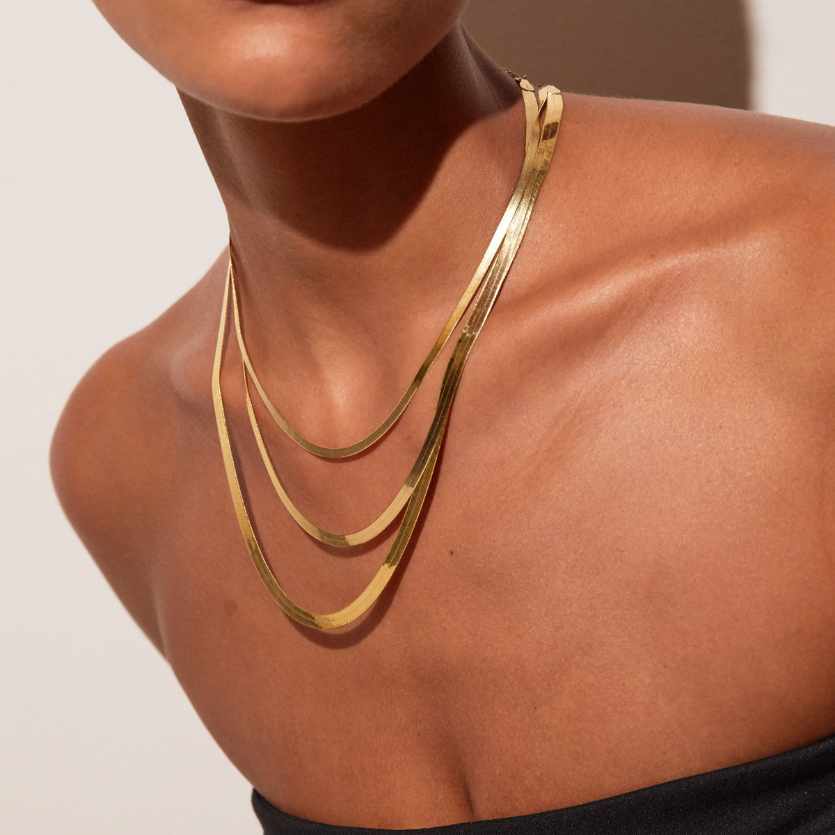 Model. Close up of woman wearing three stacked gold chains 