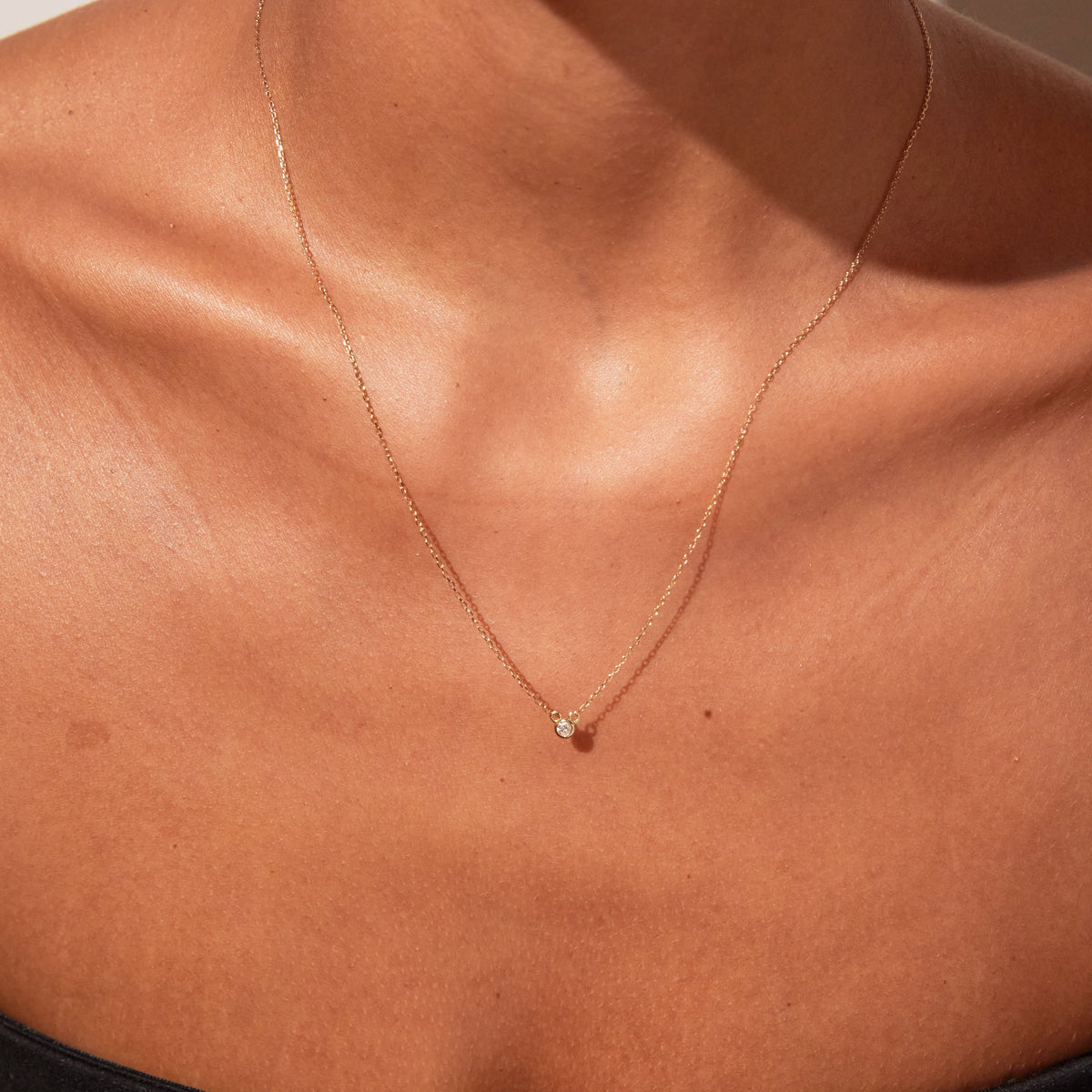 Model. A close-up lifestyle shot of a woman wearing a delicate gold diamond necklace.