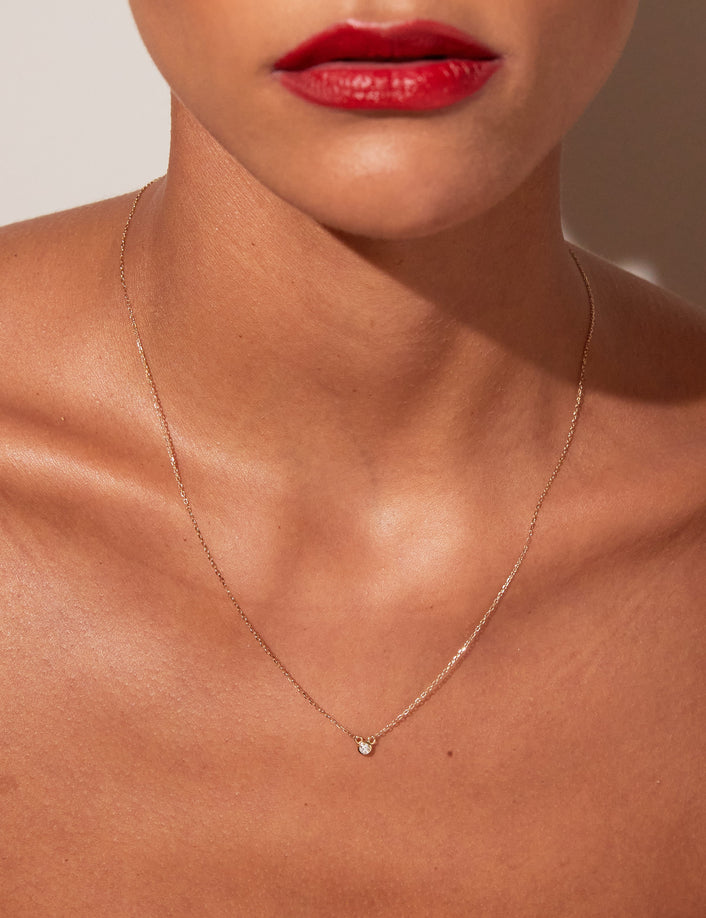 A close-up lifestyle shot of a woman wearing a delicate gold diamond necklace.