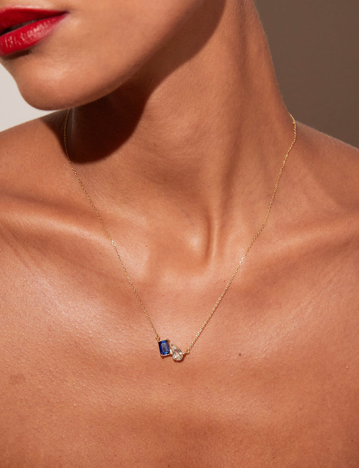 Close-up of a woman wearing a gold necklace with a blue sapphire and white topaz pendant