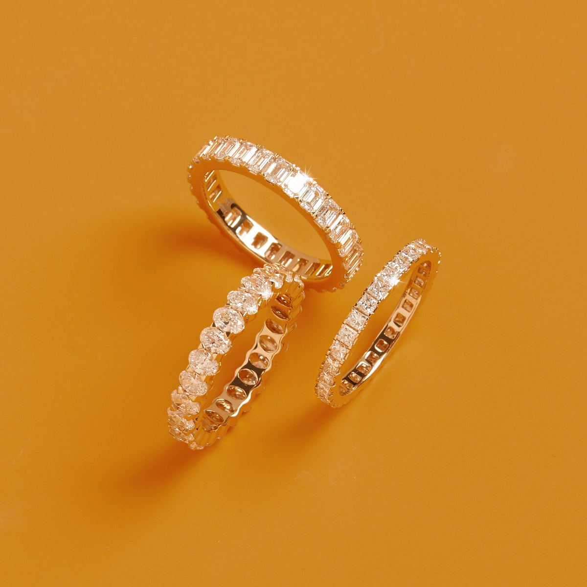 Flatlay Model  Three gold diamond eternity rings resting on a solid orange background