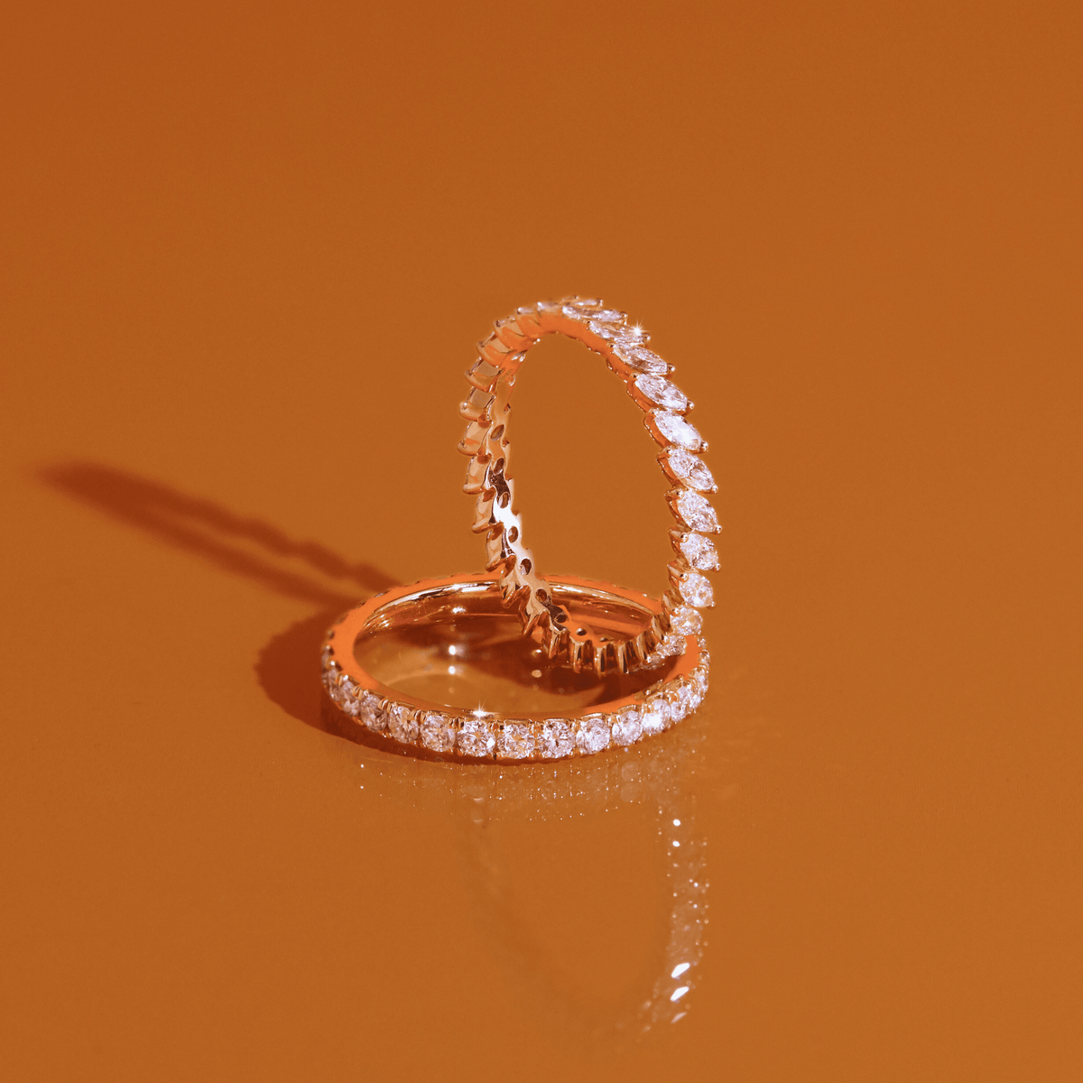 Flatlay Model Two gold diamond eternity rings resting on a solid orange background