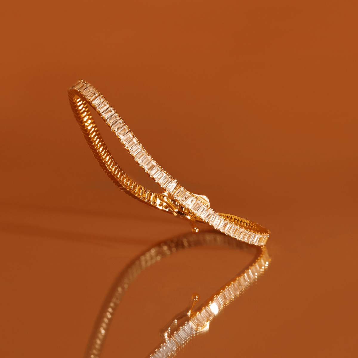Flatlay Model "Close-up of a gold tennis bracelet featuring baguette-cut white sapphires resting on a warm orange reflective surface
