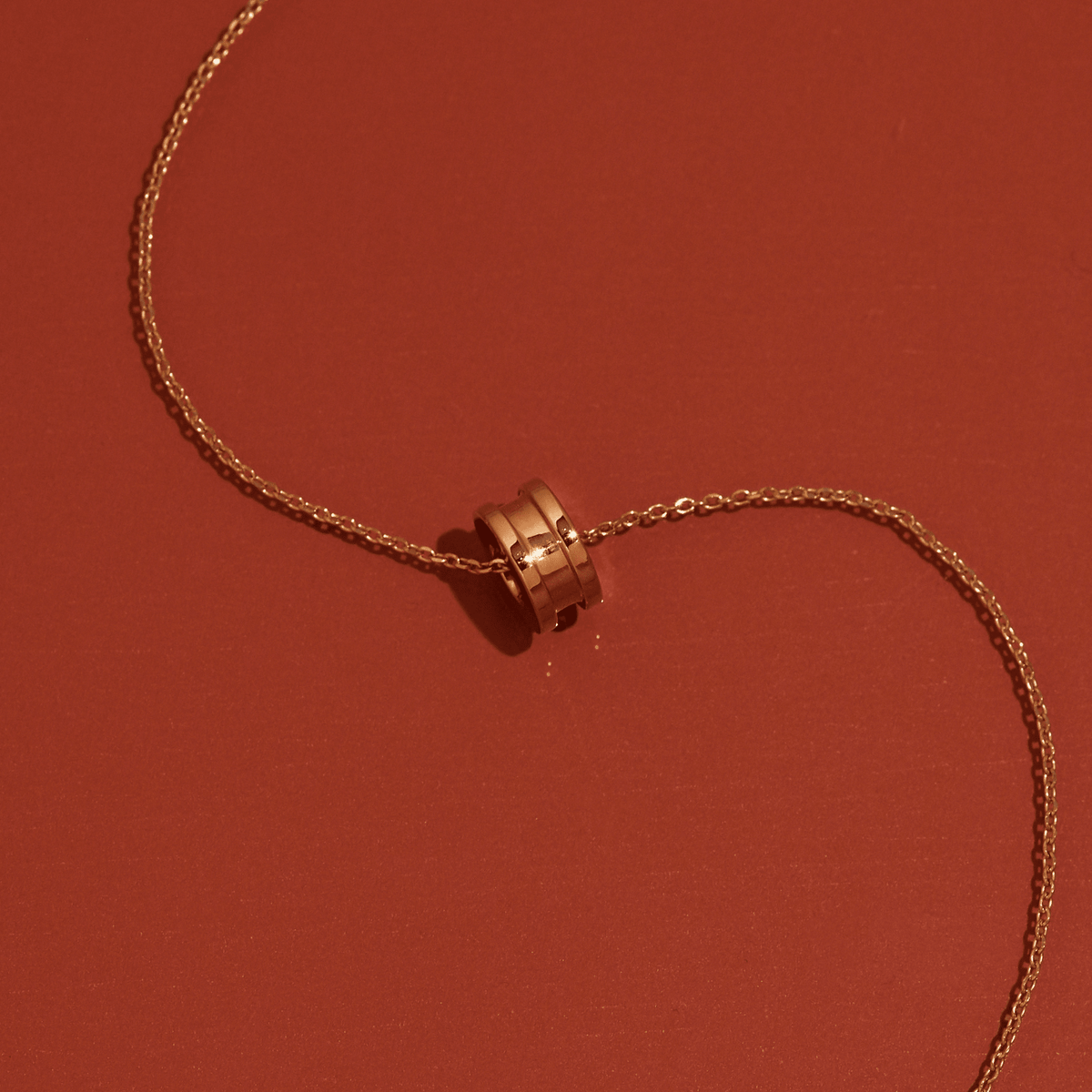 Flatlay Model Close-up of a gold column pendant necklace resting on a warm orange surface