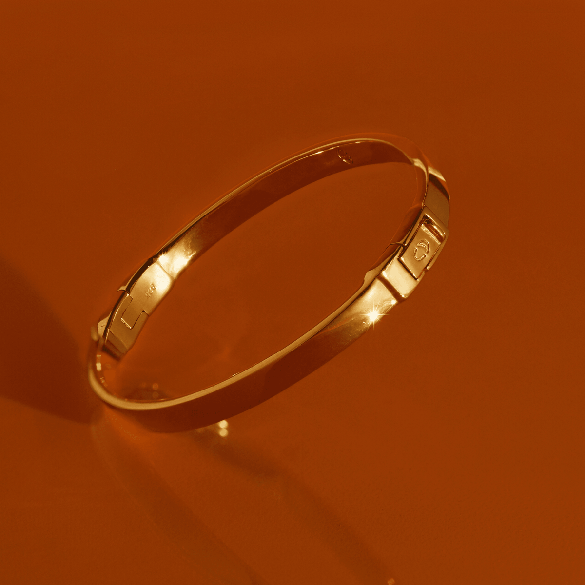 Flatlay Model. Gold hinged bracelet on orange background