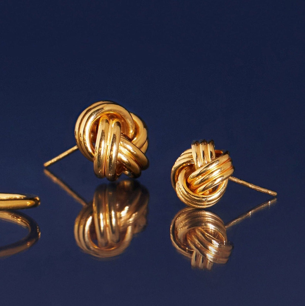 Flatlay Model gold knotted earrings on a blue background 