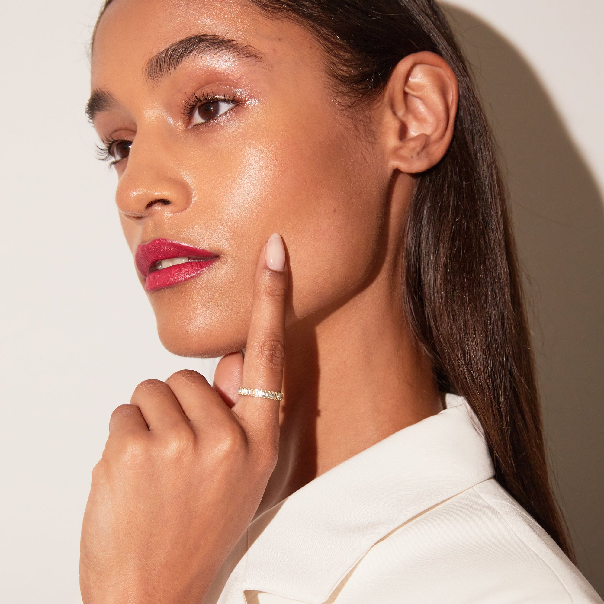 Woman with pink lipstick and a white shirt, posing with one hand on her chin.