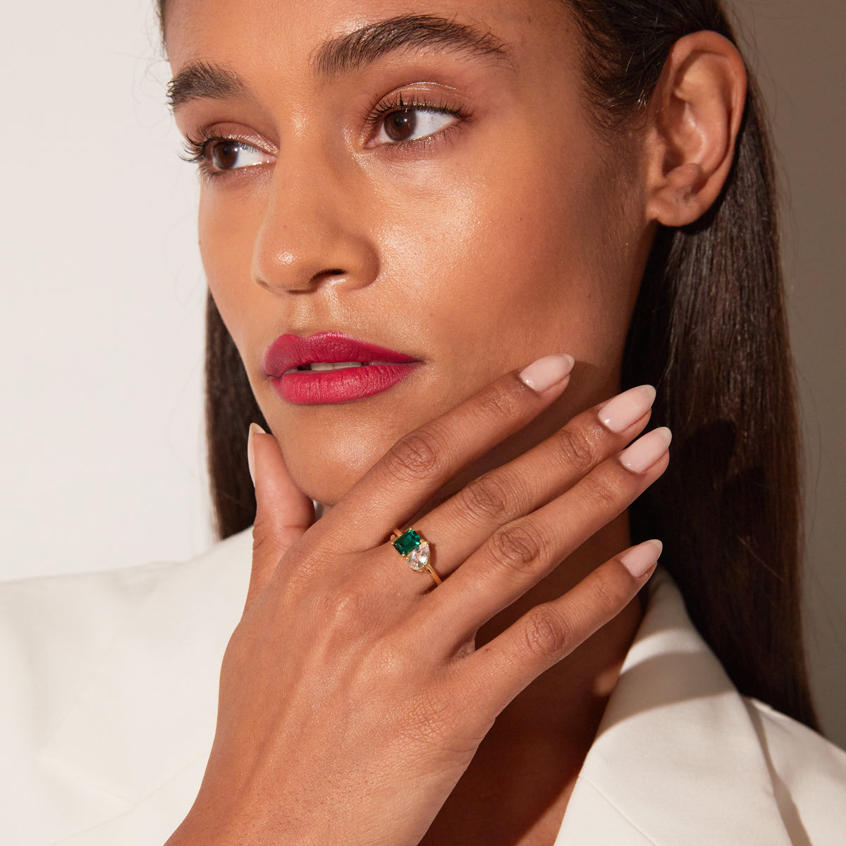 Close-up of a woman wearing a gold two-stone ring with a green and a clear gemstone.